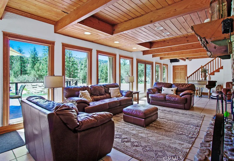 Sunstone Lodge great room with wood-beamed ceilings, stone fireplace, leather sofas and forest views