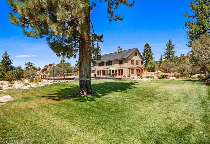 Sunstone Lodge main house and rear lawn shaded by tall pines under blue sky