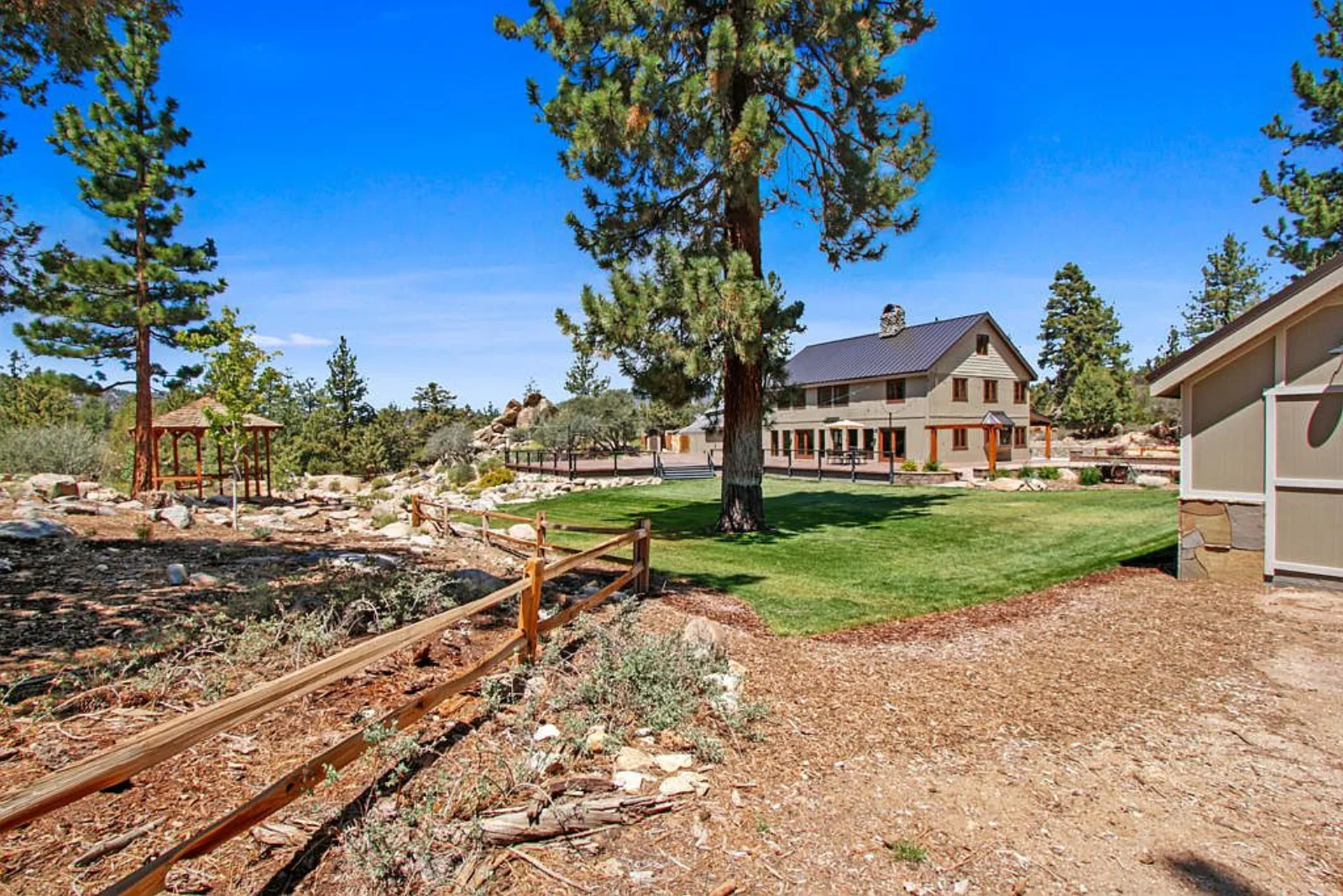 Back lawn with split rail fence, gazebo and tall pines behind the Lodge