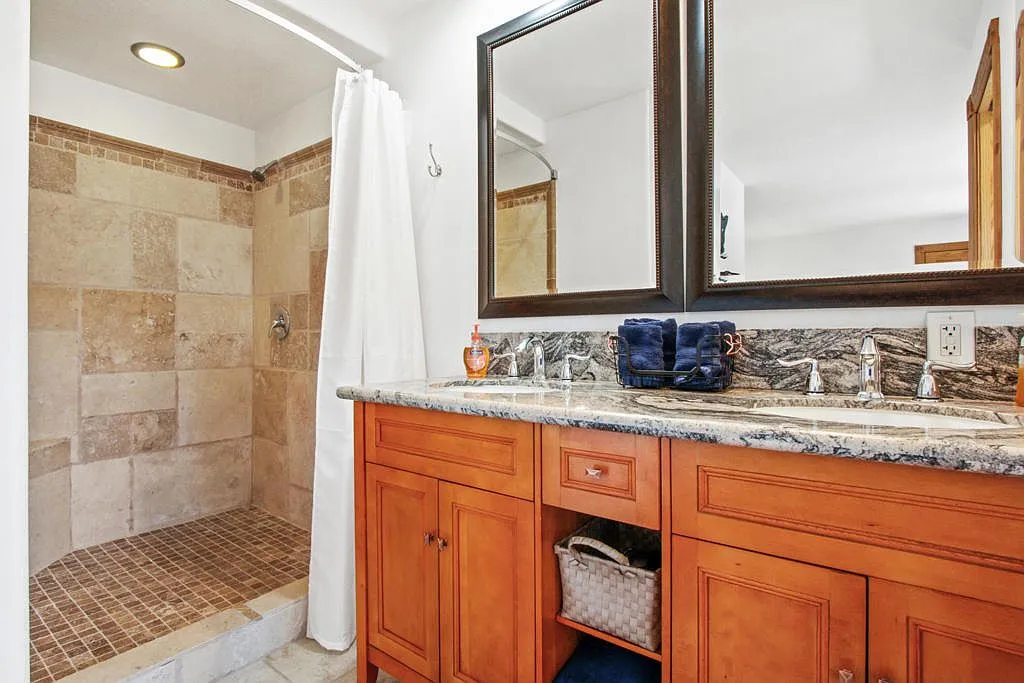 Bathroom with a granite double vanity and travertine walk in shower