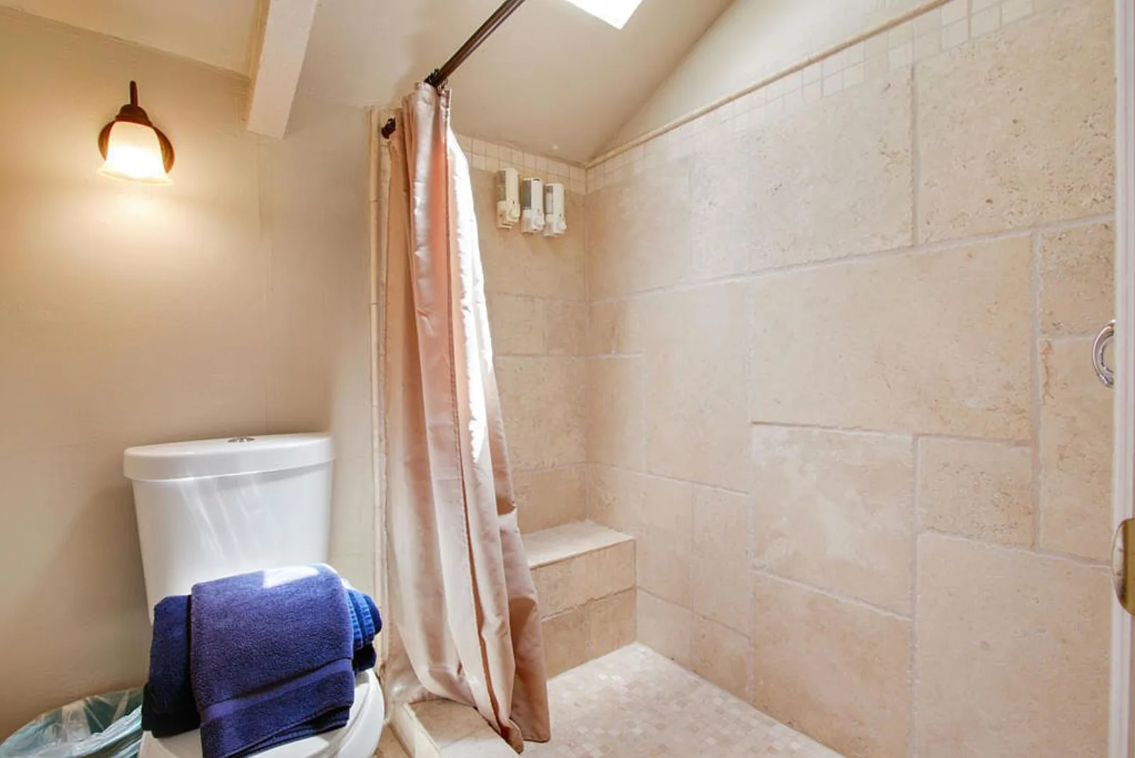Bathroom with a travertine walk in shower and bench under a skylight