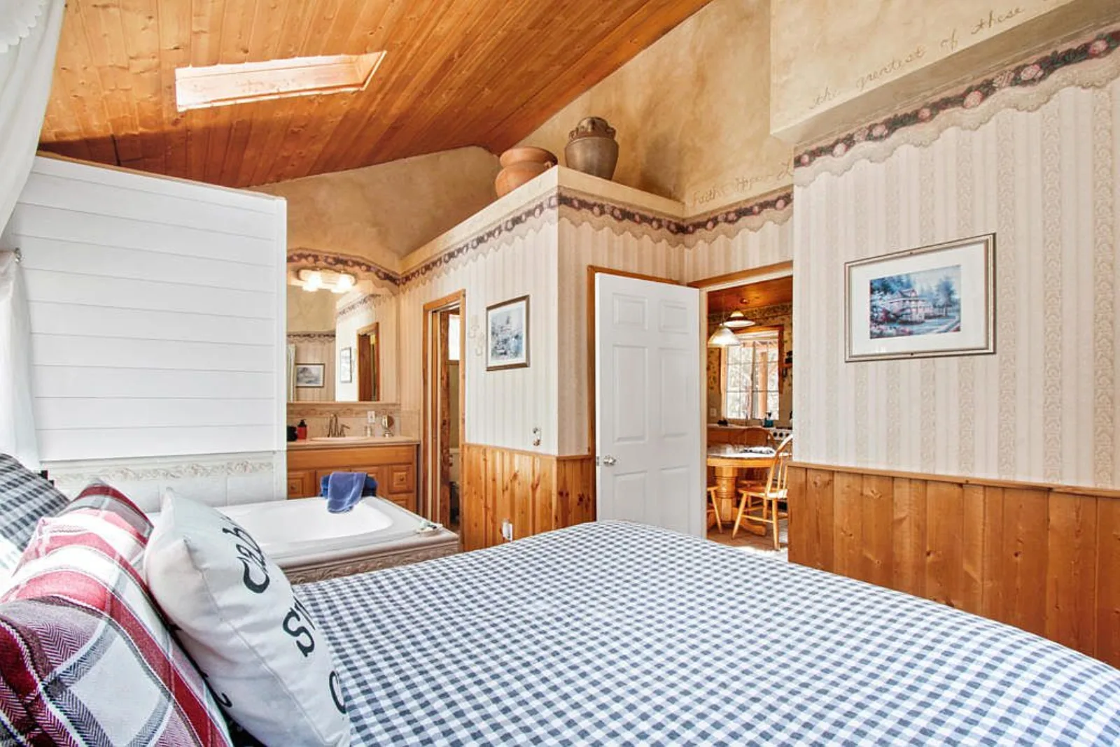 Cabin bedroom under a vaulted wood ceiling with the tub and vanity beyond