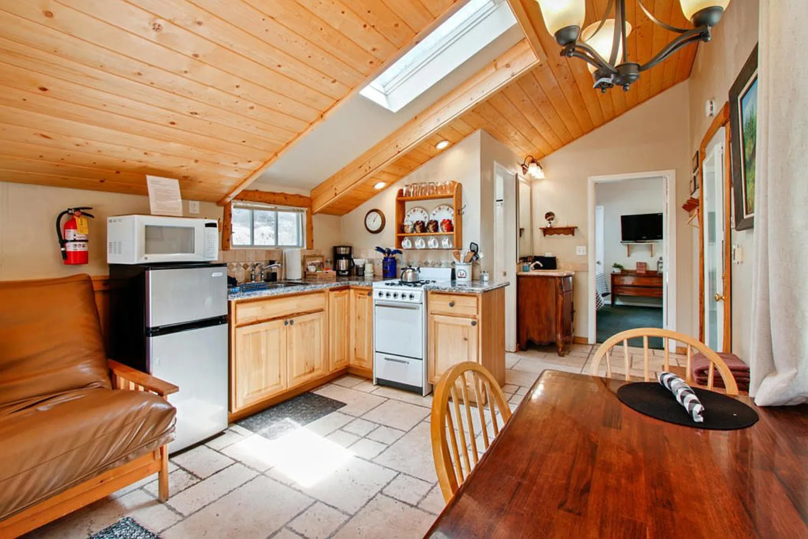 Compact cabin kitchenette with a stove and fridge under a vaulted wood ceiling