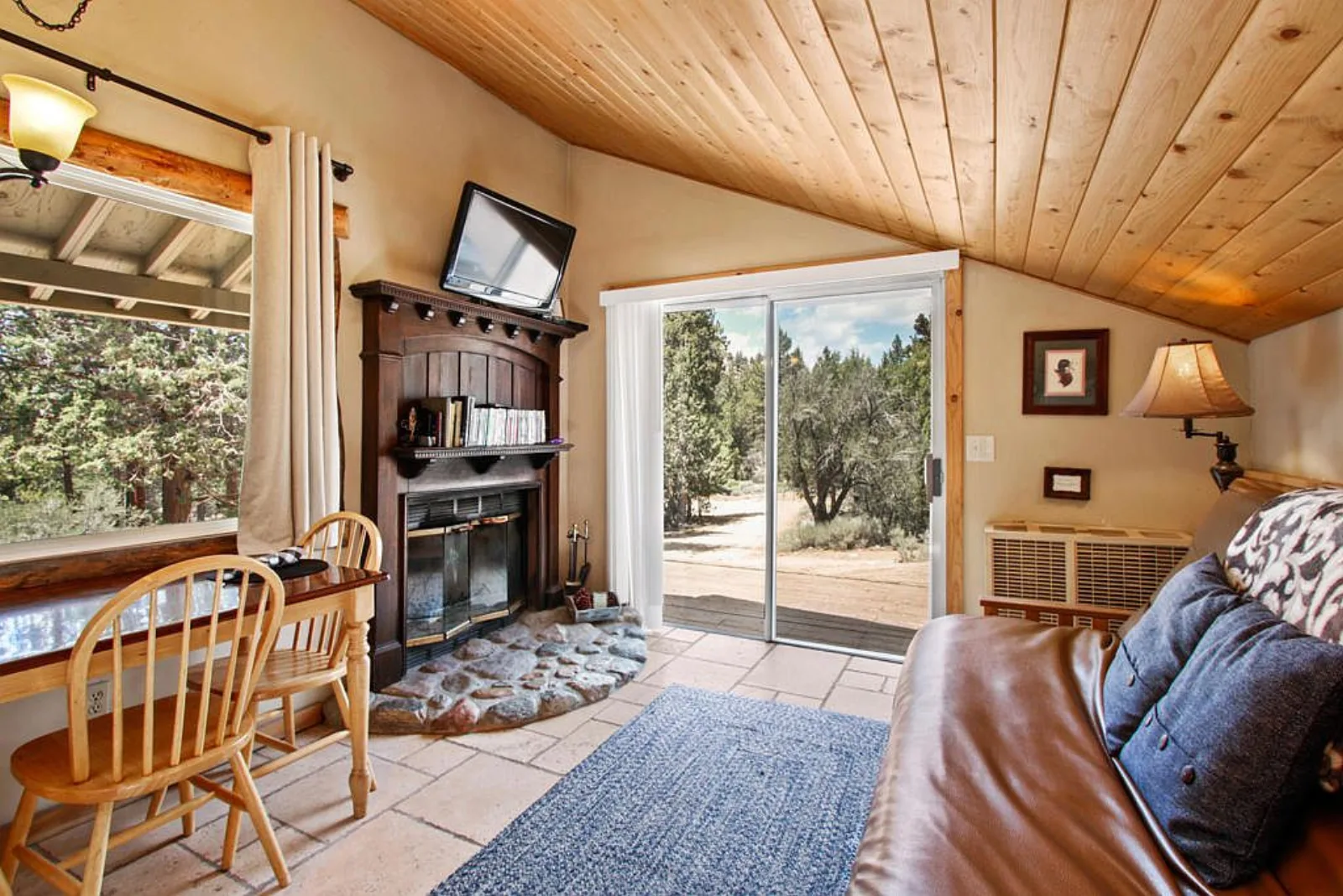 Cabin living area with a fireplace, futon and sliding door to the trees
