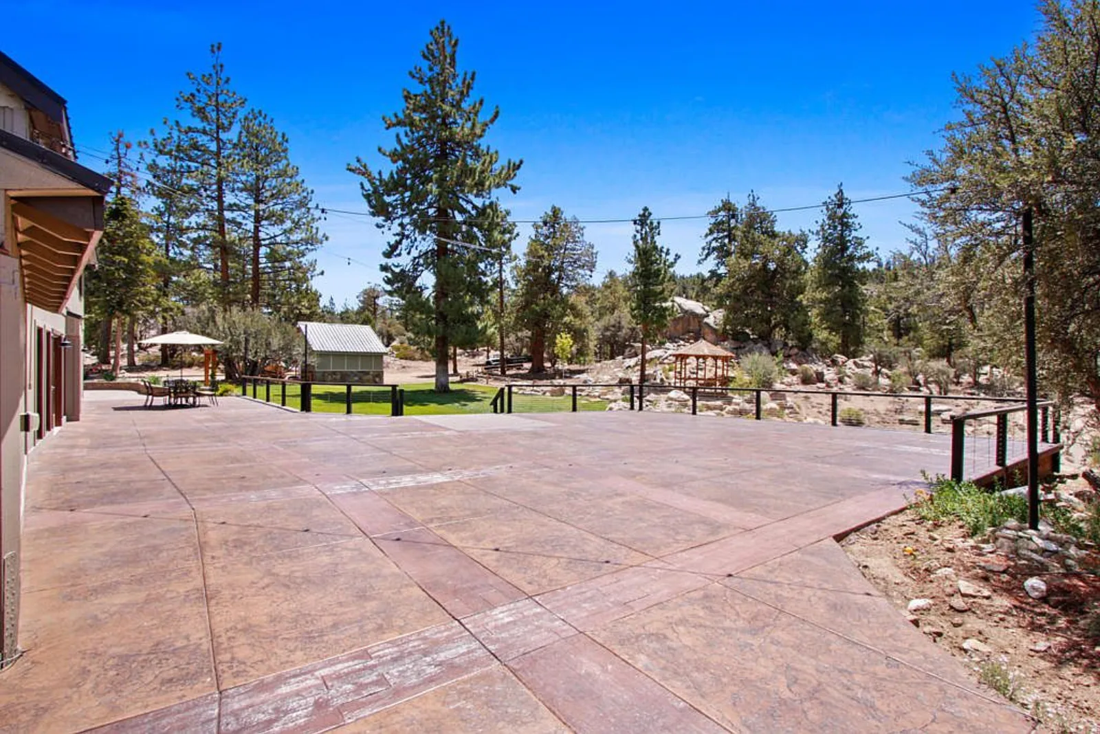 Wide stamped concrete patio overlooking the lawn, gazebos and surrounding pines
