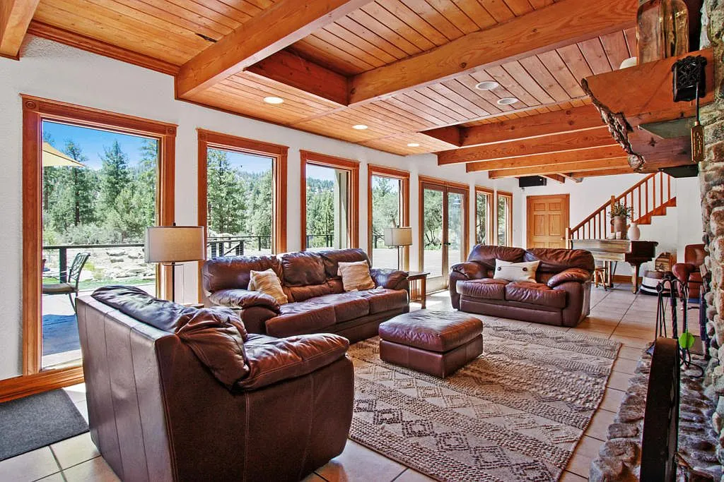 Lodge living room with forest view windows and the staircase by the stone fireplace