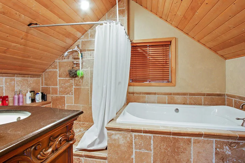 Bathroom with a travertine soaking tub and shower under a sloped wood ceiling